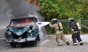 Two firefighters extinguishing a controlled fire using a water hose.