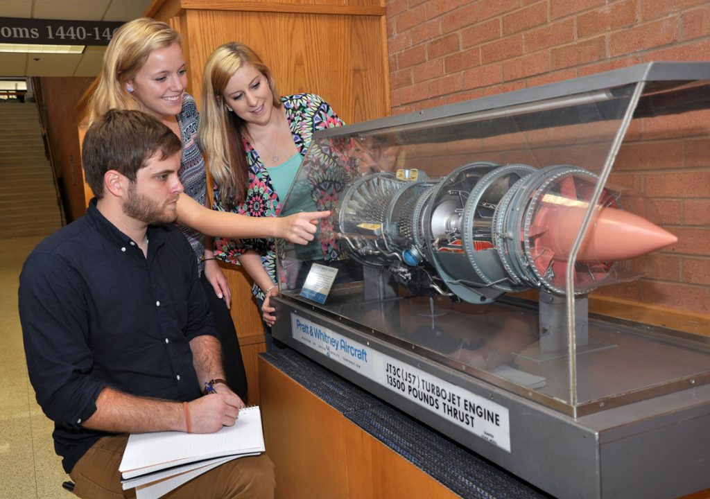 three people looking at a model of a jet engine.