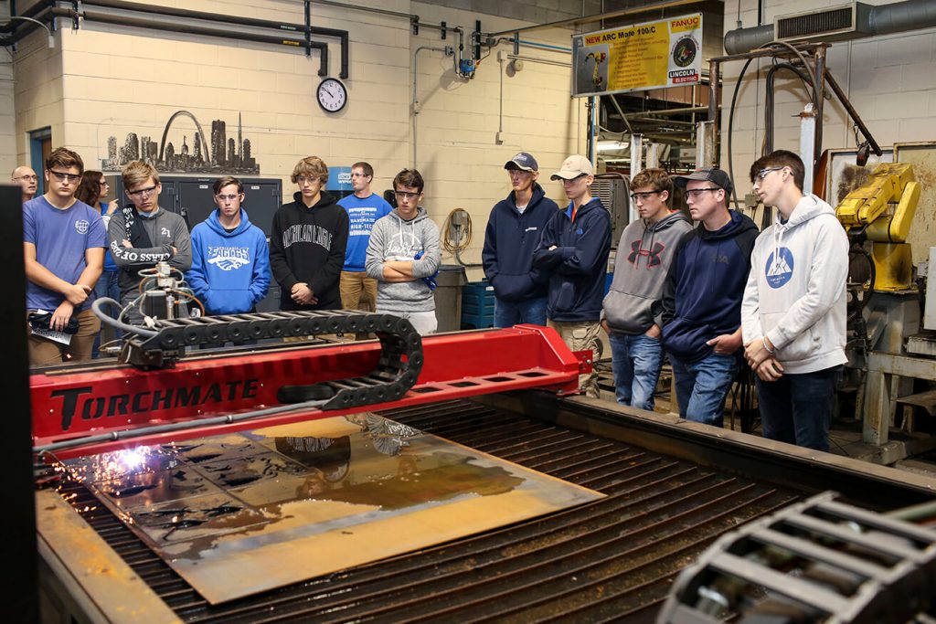 Students gather to view an automated welding machine perform cuts on 1/4 inch steel.