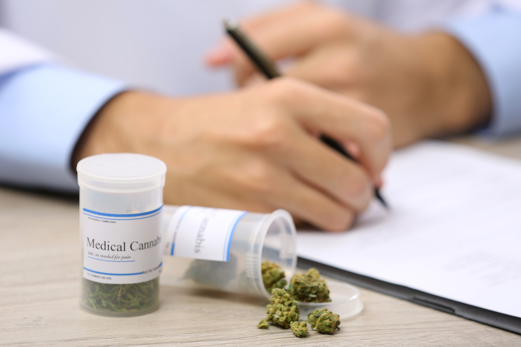 Doctor writing on prescription blank and bottle with medical cannabis on table close up