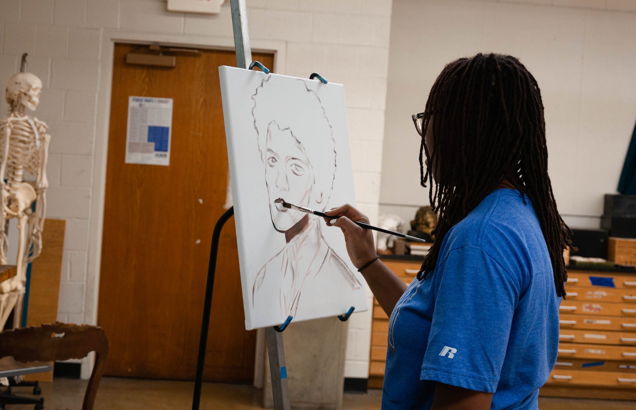 Student in painting class painting a picture of a man on canvas