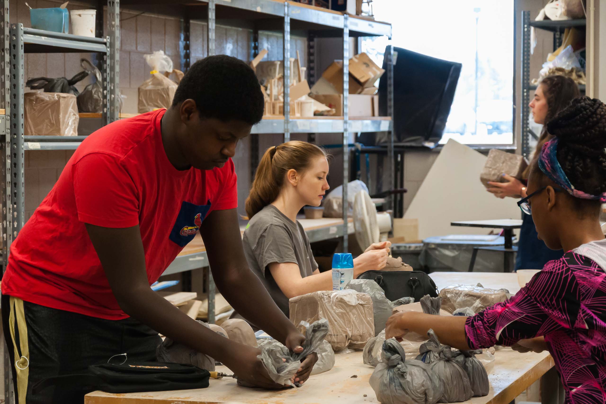 Students in ceramics class working with blocks of clay at the table together. Activity Scholarship potential