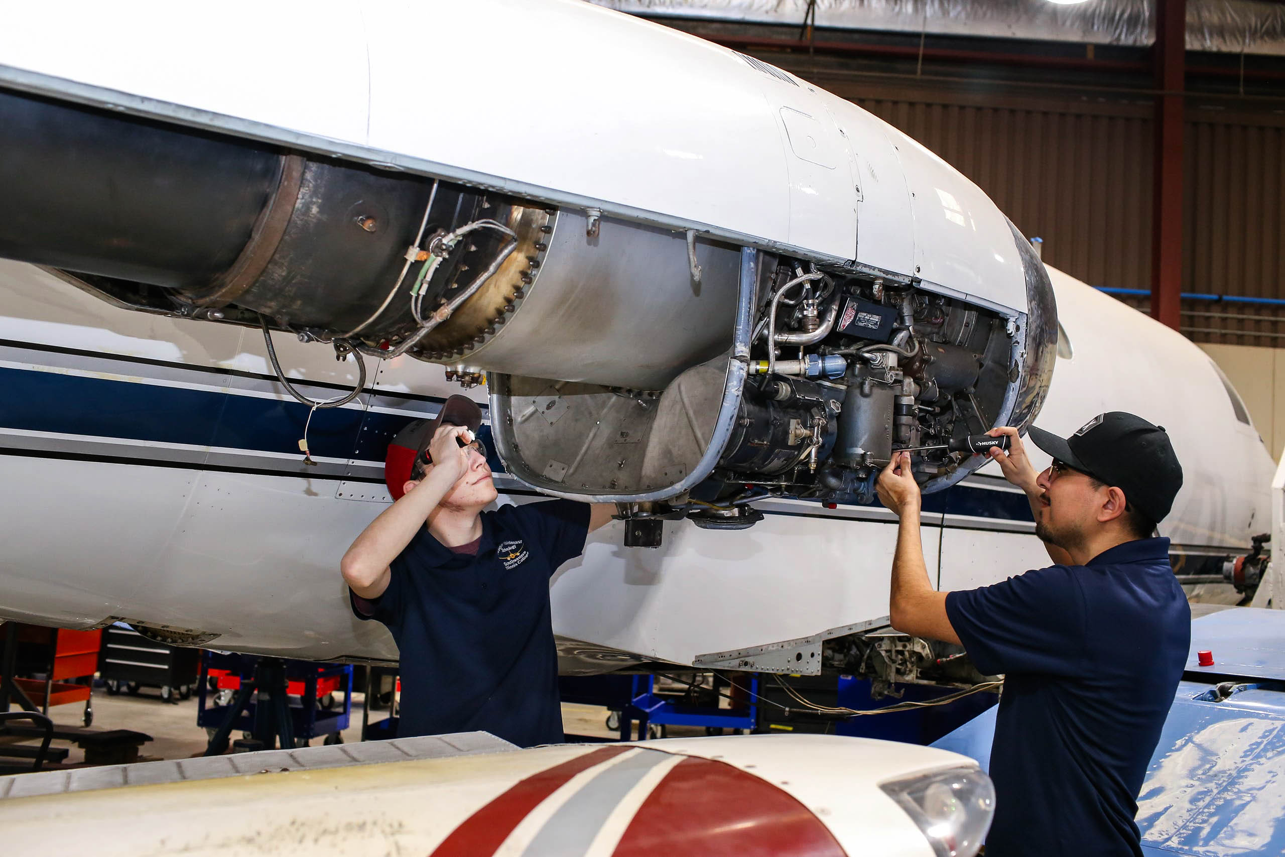 Two students in the aviation program doing overhead maintenance on a large plane engine